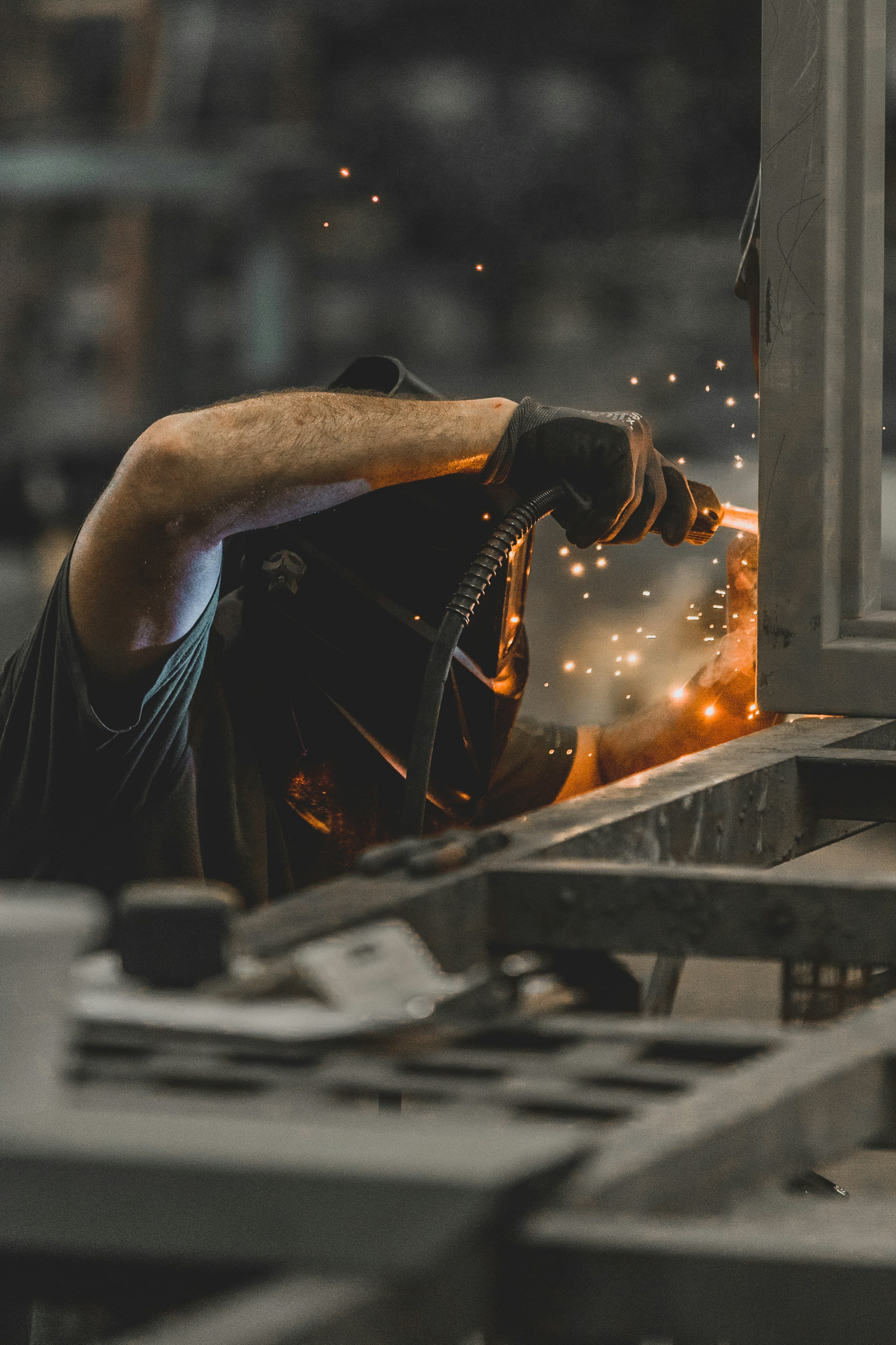 Welder in protective gear working metal with sparks on the shop floor
